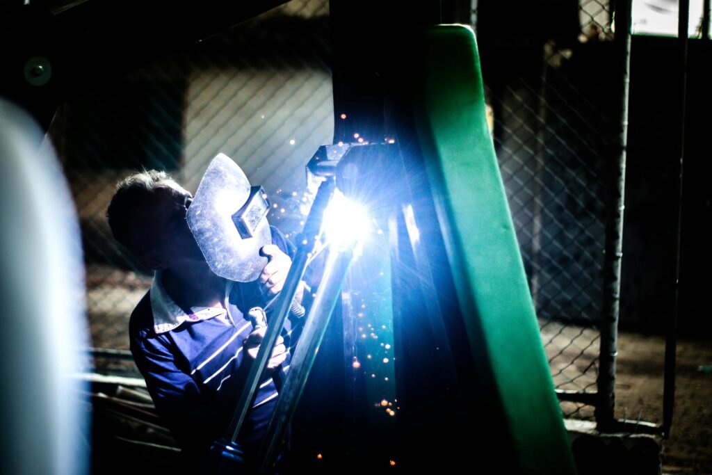 A welder at work during nighttime in an industrial setting, producing bright sparks.